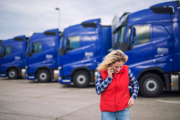 Lkw-Fahrerin telefoniert vor einer blauen Lkw-Flotte