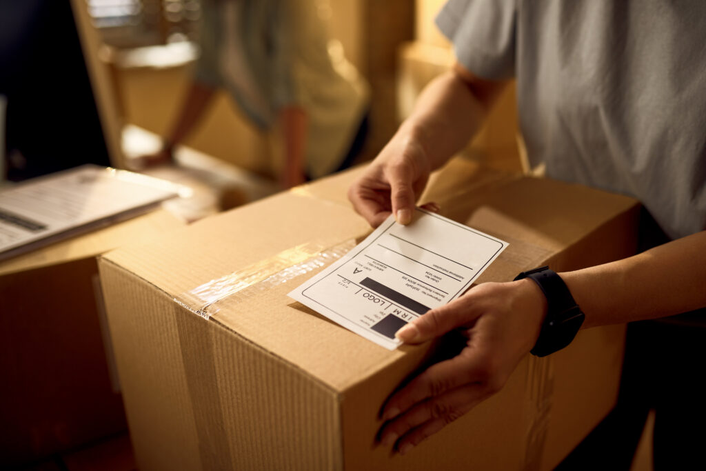 Nahaufnahme eines Kuriers, der ein Adressetikett auf einem Paket anbringt.